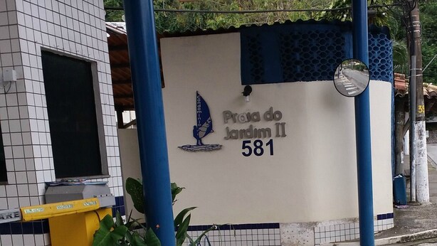Een gebouw met een betegelde gevel, een bord met de tekst 'Praia do Jardim II 581' en een overdekt gebied met blauwe pilaren.