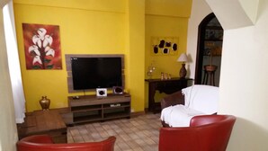 Een woonkamer met gele wanden, een flatscreen televisie, een rode bank en een rode fauteuil.