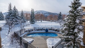 Un espace extérieur enneigé avec une piscine, entouré d’arbres et d’une clôture.