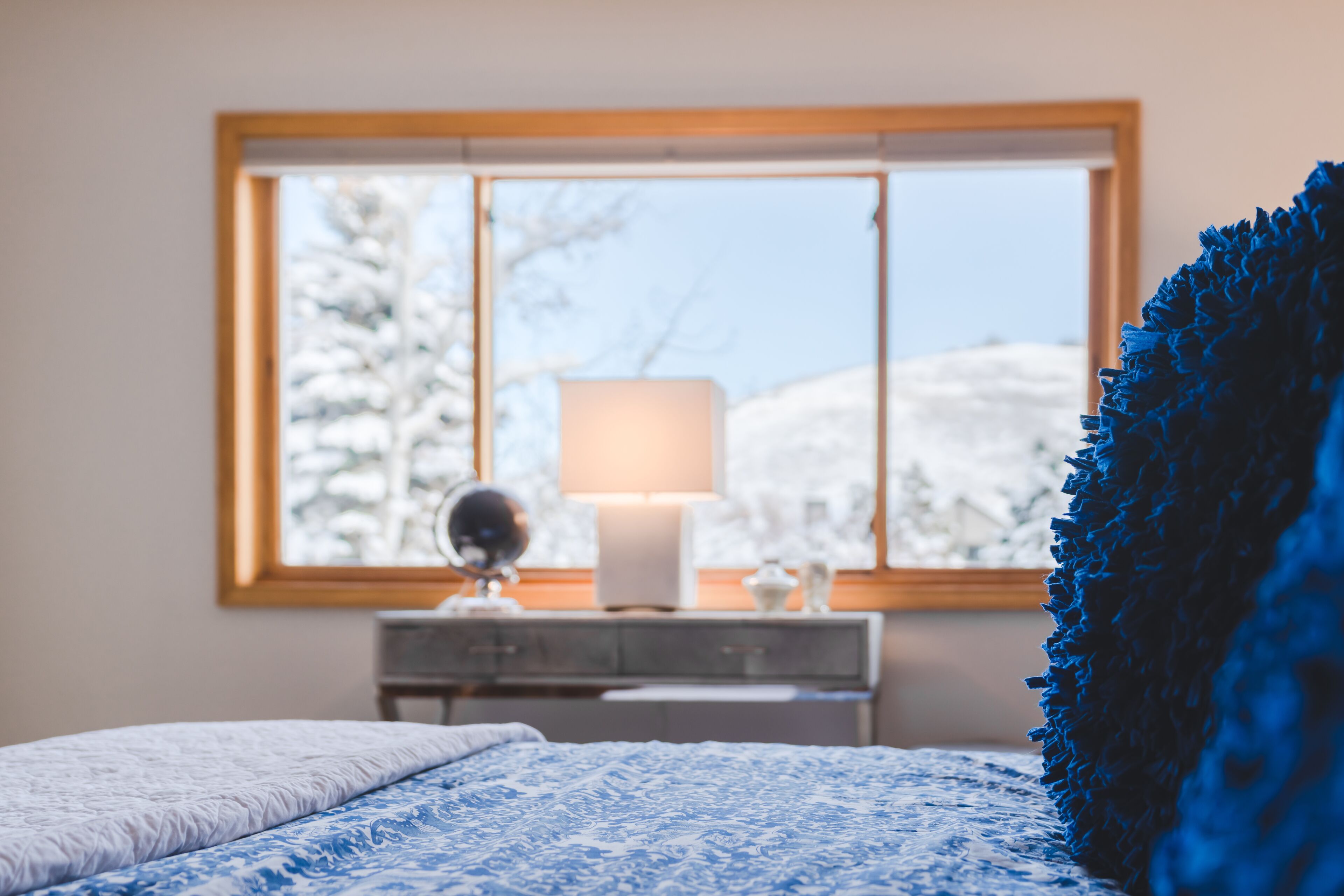 A bedroom with a bed, a dresser, a lamp, and a window with a view of snow-covered trees.