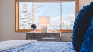 Une chambre à coucher avec un lit, une commode, une lampe et une fenêtre donnant sur des arbres couverts de neige.