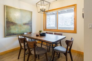 Un coin repas avec une table en bois, six chaises, un grand tableau abstrait et une fenêtre donnant sur un paysage enneigé.