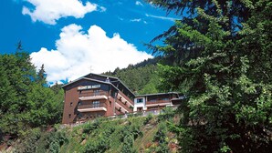 Un chalet de montagne appelé « Front de Neige », doté de plusieurs balcons et offrant une vue sur la forêt environnante.