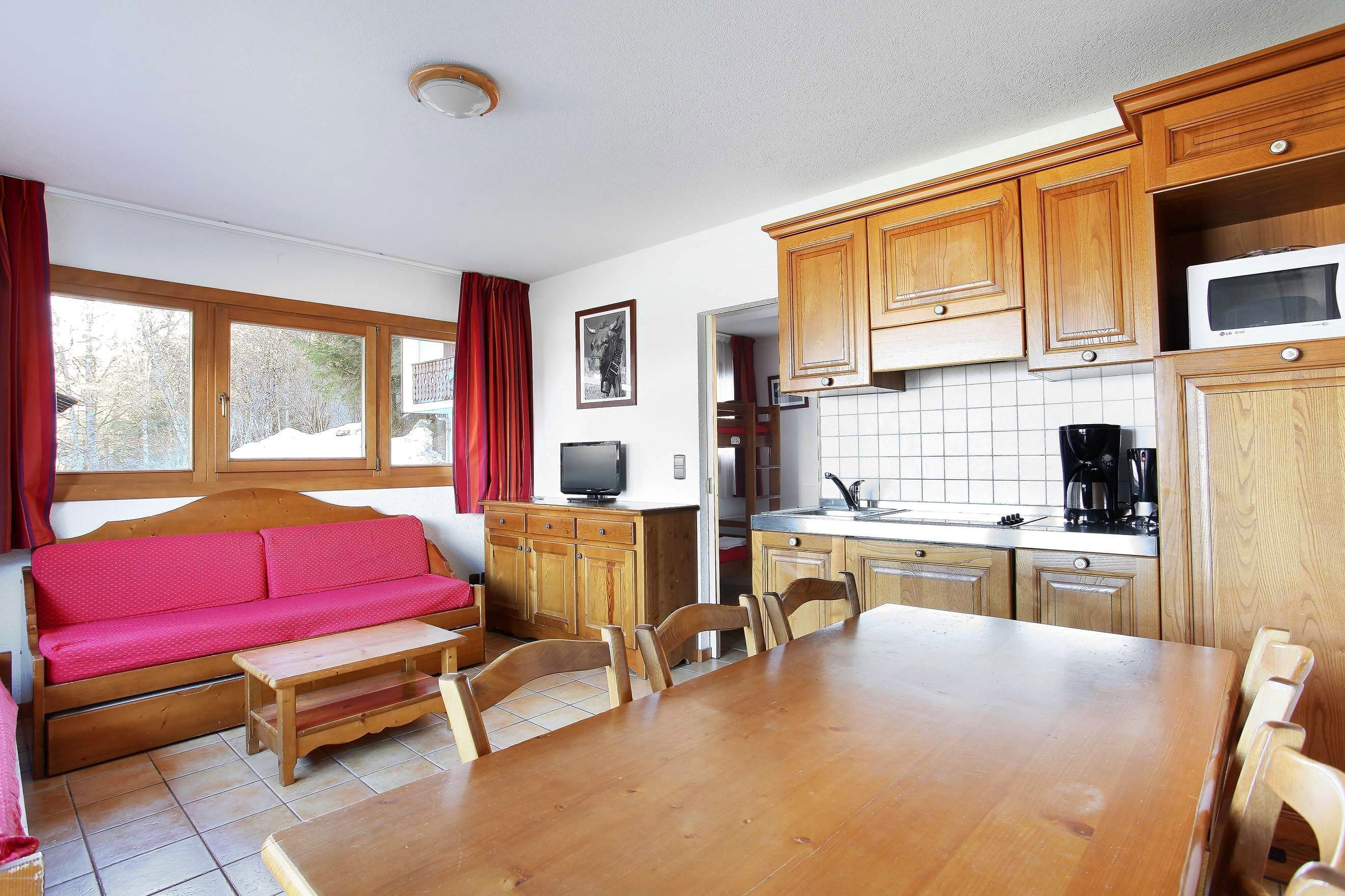 A cozy kitchen with wooden cabinets, a dining table, and a red sofa.