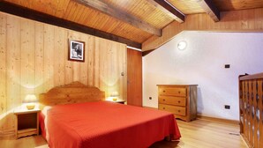 A wooden-paneled bedroom with a bed, bedside lamps, a dresser, and a wooden ceiling.
