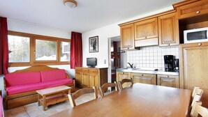 A cozy kitchen with wooden cabinets, a dining table, and a red sofa.