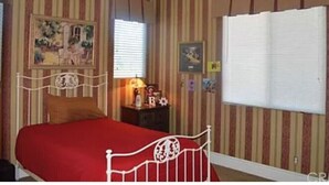 Quarto com cama, mesa de cabeceira, ventilador de teto e papel de parede listrado.