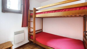 A bunk bed with a red mattress, a window with curtains, and a wall-mounted heater.