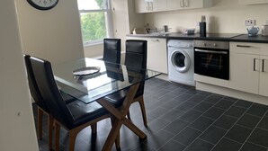 Una cucina moderna con un tavolo da pranzo in vetro, due sedie, una lavatrice e una sveglia appesa al muro.