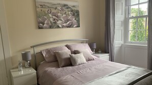 Una camera da letto con un letto, comodini, una lampada, un quadro e una finestra con tende.