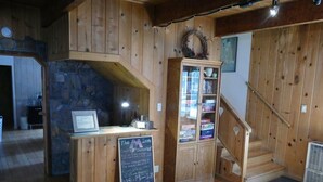Un interior de fusta amb una paret de pedra, un taulell de fusta amb un menú al pissarra, un armari amb frontissa de vidre i una escala.