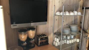 A kitchen with a flat-screen TV, a toaster, and shelves with plates and cups.