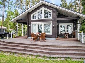 A two-story wooden house with a covered porch, a dining area with chairs and a table, and a staircase leading to the entrance. - Villa ina by Interhome (Evijärvi)