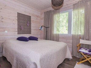 A bedroom with a bed, a bedside table, a lamp, and a window with curtains. - Villa ina by Interhome (Evijärvi)