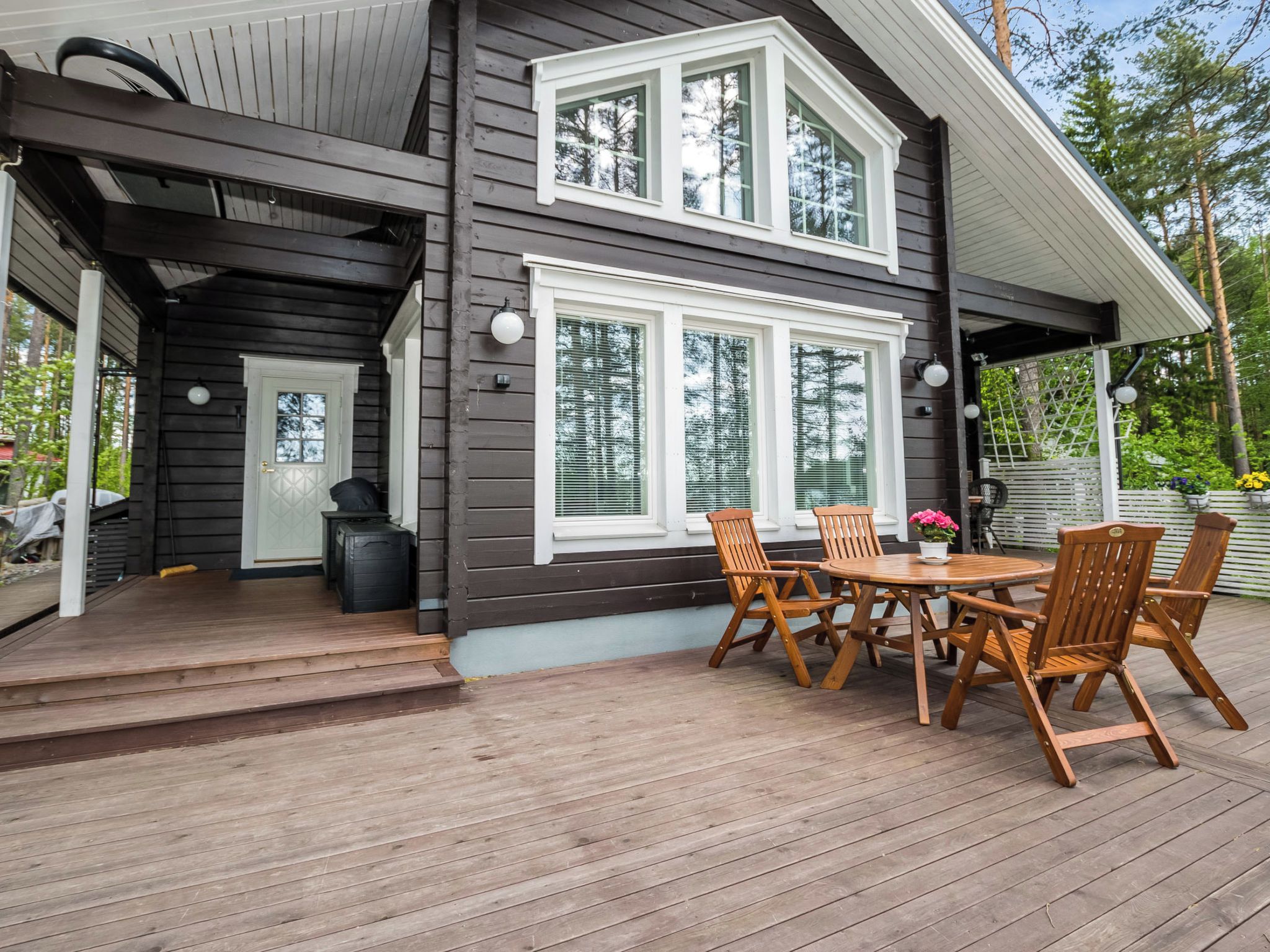 Ein zweigeschossiges Haus mit einer Terrasse, Sitzgelegenheiten im Freien und einer Garage.