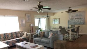 Ein Wohnzimmer mit Sofa, Sesseln, Couchtisch, Essbereich mit Stühlen und Deckenventilatoren.
