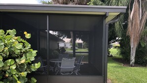 Eine überdachte Terrasse mit Tisch und Stühlen, umgeben von viel Grün.