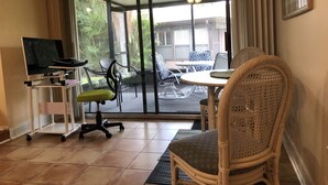 Ein Zimmer mit einer Glastür, die auf eine Außenpatio führt. Im Inneren befinden sich ein Schreibtisch mit einem Computer, ein Stuhl und ein Esstisch mit Stühlen.
