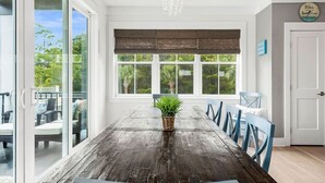 A dining area with a wooden table, blue chairs, a potted plant, and a view of greenery outside.
