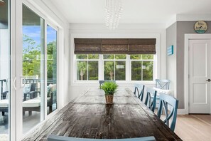 Comedor con mesa de madera, sillas azules, planta en maceta y vistas al verdor exterior.