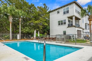 A swimming pool with lounge chairs and a two-story building with balconies.