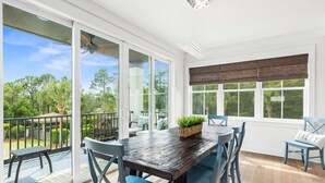 A spacious balcony with a wooden table and chairs, a wicker basket, and a view of greenery.