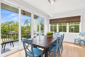 A dining area with a wooden table and blue chairs, large windows with a view of greenery, and a ceiling fan.