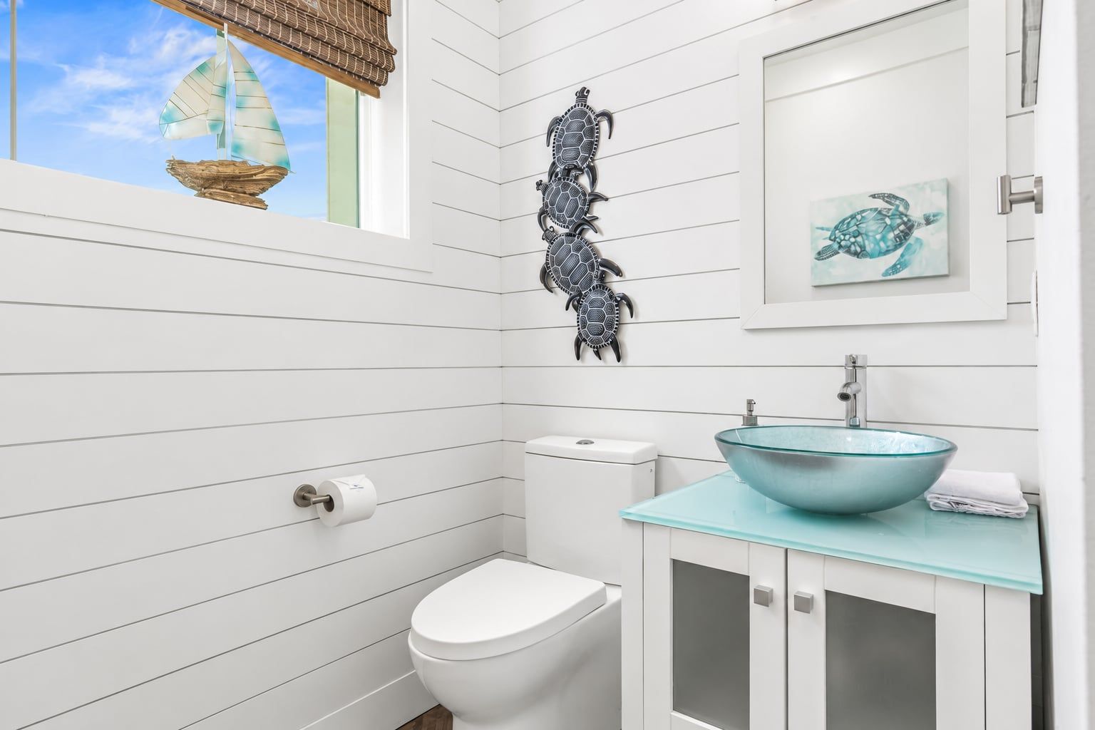 Un baño con inodoro, lavamanos de vidrio, toalla y un adorno de pared con forma de tortuga.