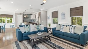 A spacious living room with a blue sofa set, a coffee table, and a kitchen in the background.
