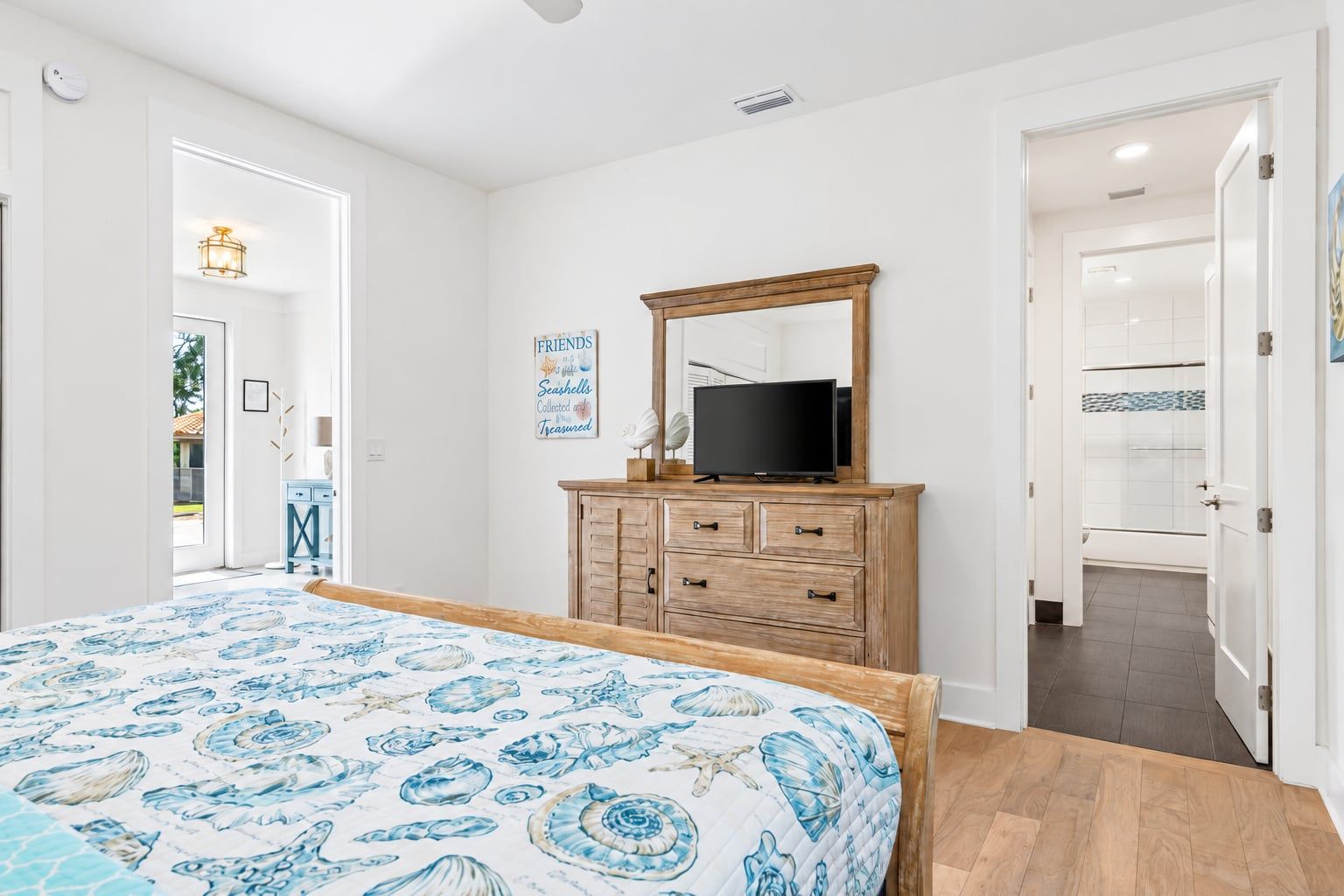 A bedroom with a bed, a dresser, a television, and a door leading to a bathroom.