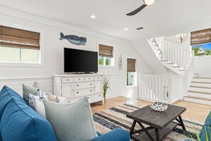 A modern living room with a flat-screen TV, white cabinetry, a staircase, and a large window.