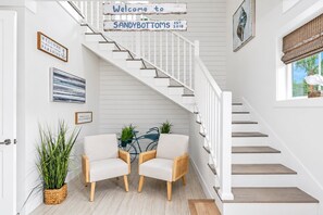 A staircase with a sign reading 'Welcome to SANDYBOTTOMS EST. 2018' and two wicker chairs in front.
