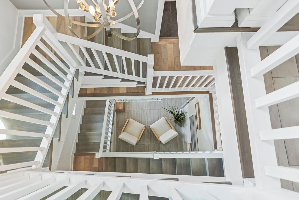 A modern interior with a spiral staircase, wooden flooring, and a seating area with two chairs and a plant.