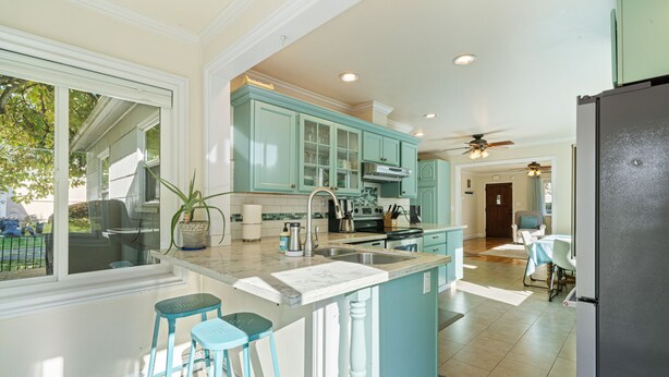 A modern kitchen with teal cabinets, a large island, and a black refrigerator. - Cottage near Vancouver Lake! Cozy, Clean, & Comfortable w/ new Pickleball Court! (Vancouver)