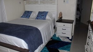 A neatly made bed with a white headboard and blue patterned pillows, a small bedside table with drawers, and a blue and white patterned rug. - A single family home in a secure gated community where you can feel at home (Florence Hall Village)