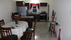 A compact kitchen with a dining area, featuring a refrigerator, stove, and a small island with a sink. - A single family home in a secure gated community where you can feel at home (Florence Hall Village)
