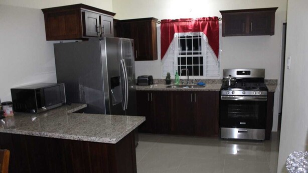 A kitchen with dark wooden cabinets, a stainless steel refrigerator, a stove, and a microwave. - A single family home in a secure gated community where you can feel at home (Florence Hall Village)
