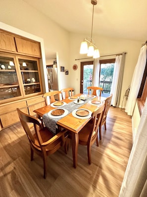 A dining area with a wooden table, chairs, and a kitchen in the background. - Peaceful Island Retreat on Foys Lake MT – Hot Tub, Private Dock, Beach & Kayaks! (Kalispell)