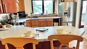A modern kitchen with wooden cabinets, a stainless steel refrigerator, and a large island with chairs.