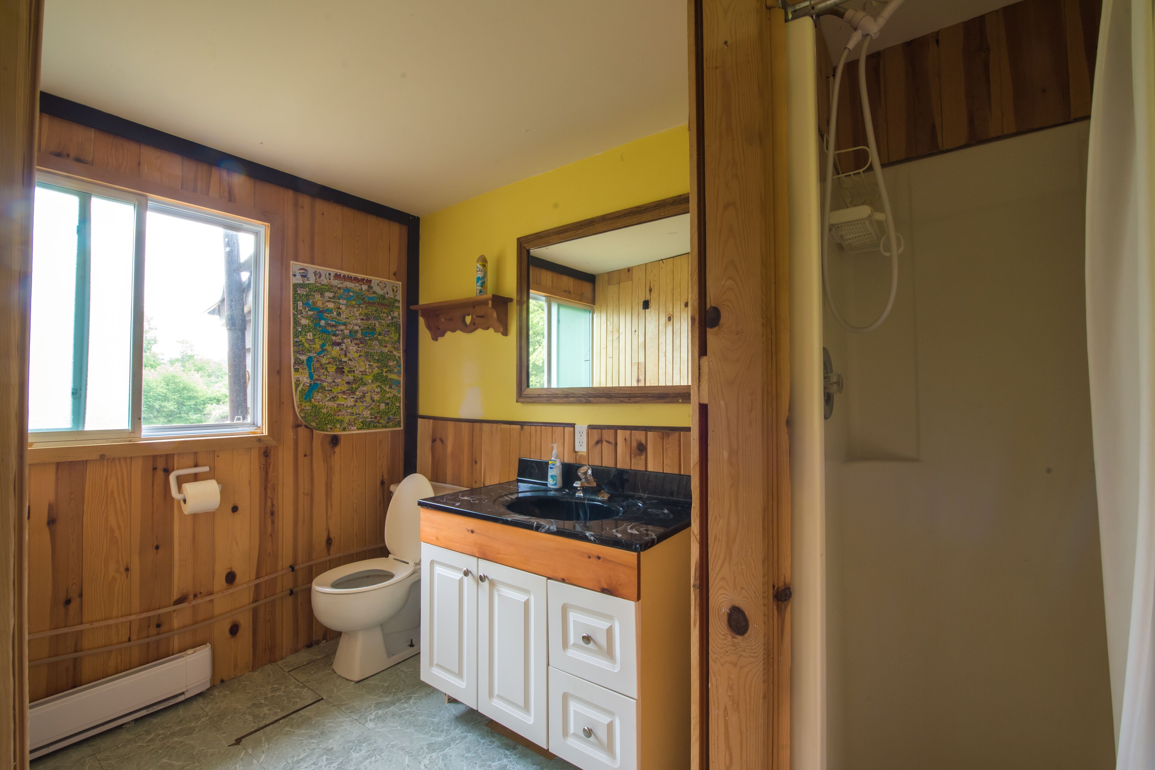 A bathroom with wooden walls, a white toilet, a black sink with a wooden countertop, and a shower area.