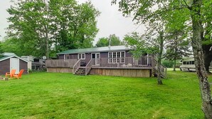 A wooden house with a deck, surrounded by a grassy yard and trees. - Beautiful 3 Bdrm + Bunkie waterfront cottage near Gull Lake (Minden Hills)