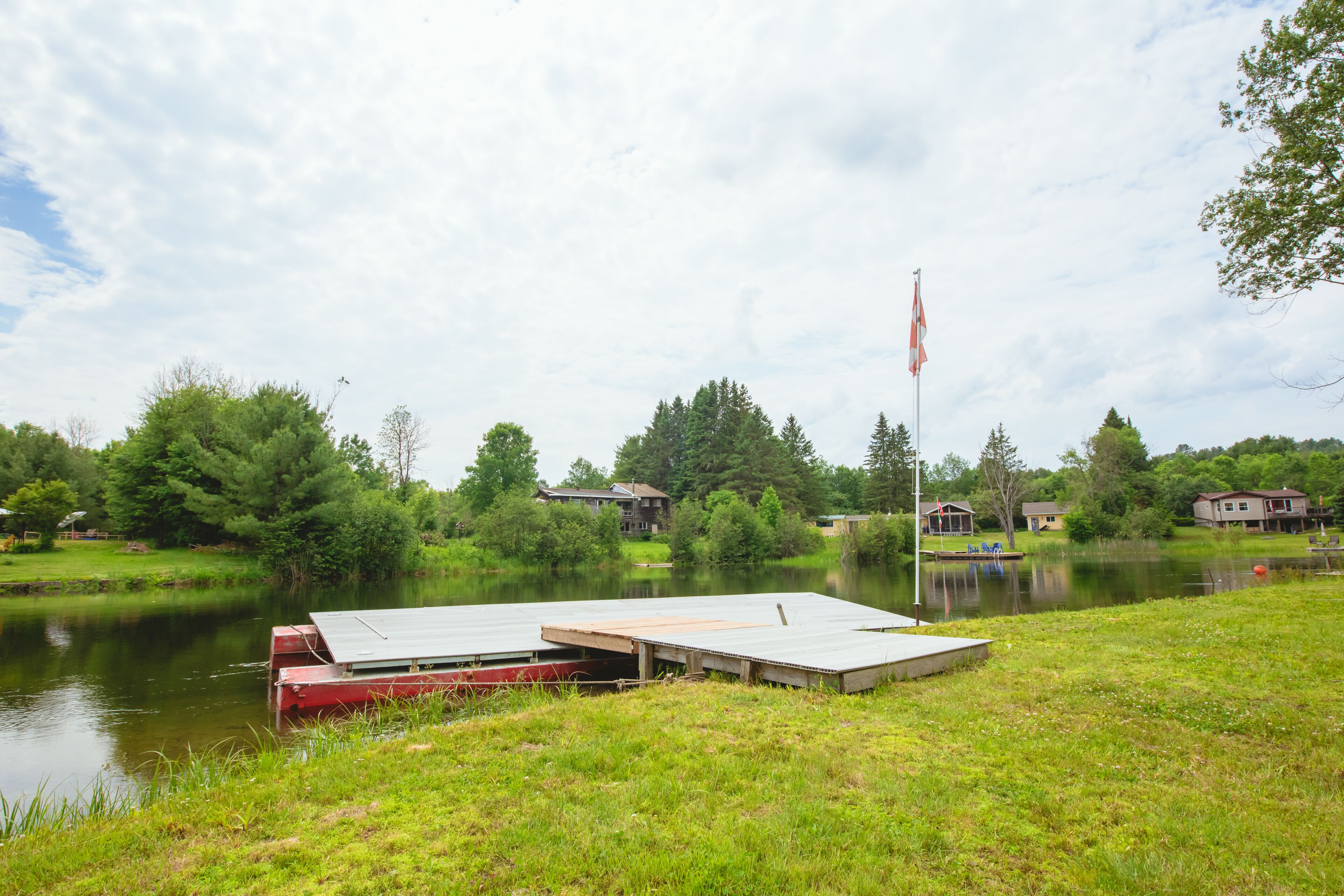 A dock extending into a calm lake with a grassy area in the foreground and houses in the background.