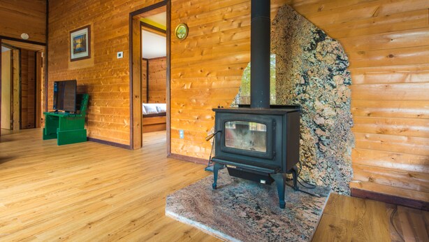 A wooden cabin interior with a stone fireplace, wooden floors, and a green chair. - Beautiful 3 Bdrm + Bunkie waterfront cottage near Gull Lake (Minden Hills)