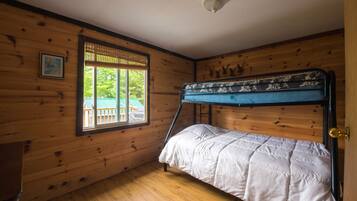 Une chambre dans un chalet en bois, avec un lit superposé, une fenêtre donnant sur un paysage verdoyant et un luminaire au plafond.