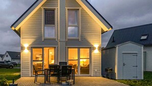 Ein zweistöckiges Haus mit einer großen Veranda, einem Essbereich mit Stühlen und Tisch sowie einer angebauten Garage rechts.
