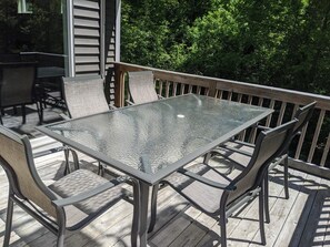 A glass-top table with metal frames and cushioned chairs on a wooden deck.