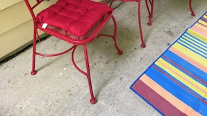 Ein rotes Metall-Stuhl- und Tischset vor einer gelben Wand, mit einem Blumentopf auf dem Tisch.