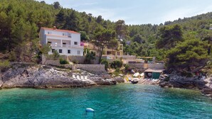 Une propriété située sur la côte, dotée d’un grand bâtiment, d’un rivage rocheux et d’une eau turquoise cristalline.
