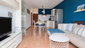 A modern living room with a flat-screen TV, a sofa, and a dining area with chairs and a table.