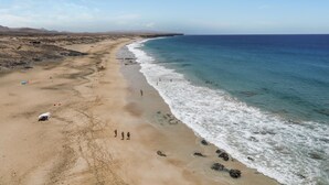 A beach with clear blue waters, a sandy shore, and distant mountains.